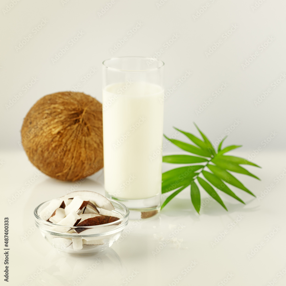 Natural non diary coconut milk. Vegan food composition with glass of coconut milk, coconut and palm leaves on a white table. Still life with vegan healthy product Natural non diary coconut milk. Vegan food composition with glass of coconut milk, coconut and palm leaves on a white table. Still life with vegan healthy product