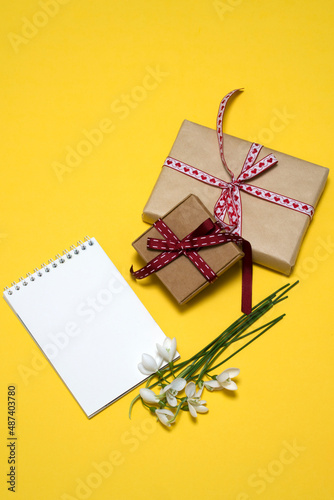 on a yellow background a bouquet of white snowdrops, two gift boxes, a notepad. card, congratulations on March 8