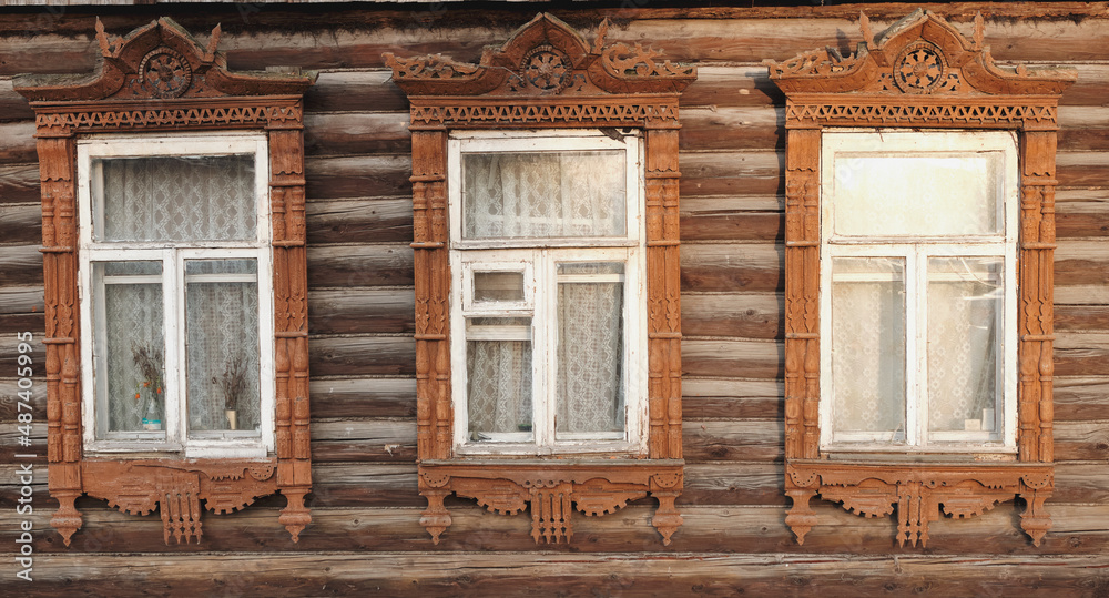 The old window of a rustic Russian wooden house is richly decorated with carvings in an old Russian city. The old window of a rustic Russian wooden house is richly decorated with carvings in an old Russian city.