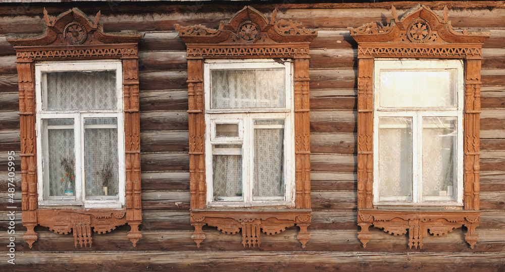 The old window of a rustic Russian wooden house is richly decorated with carvings in an old Russian city.