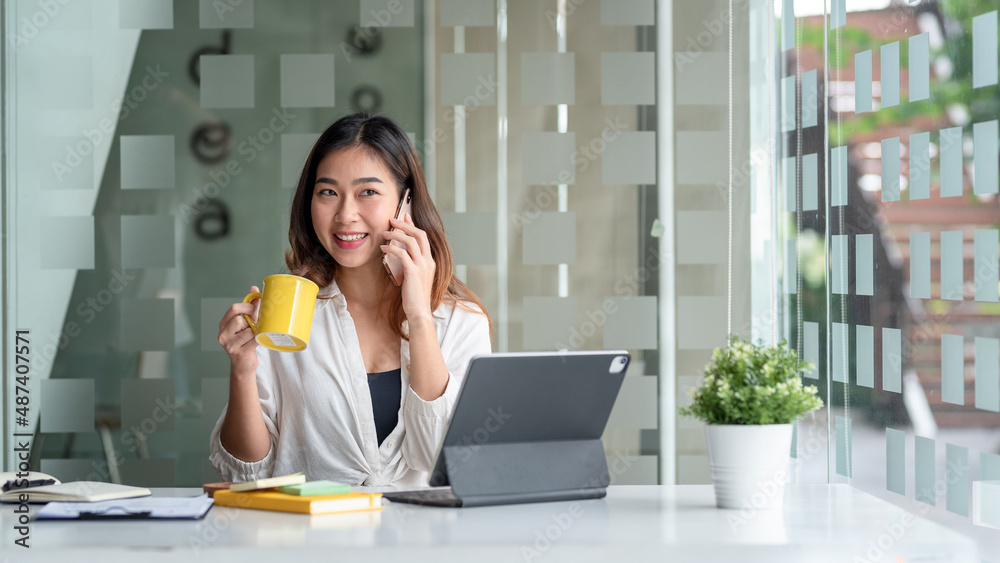 Young Asian businesswoman taking on the phone with customers while drinking coffee. Young Asian businesswoman taking on the phone with customers while drinking coffee.