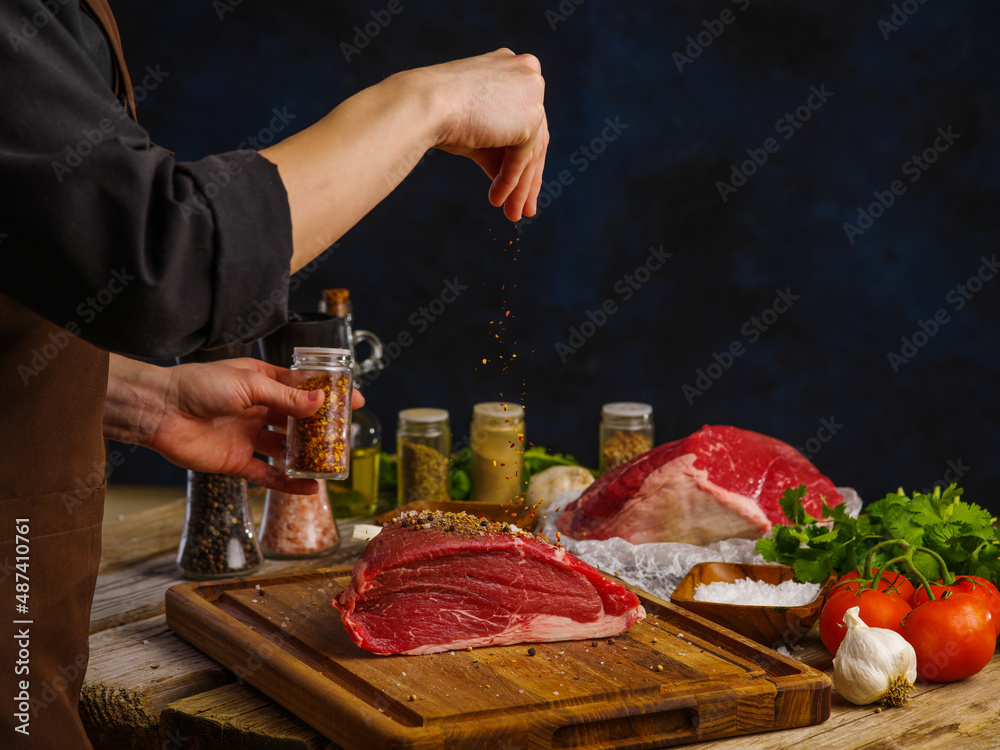 Cooking dishes from pork, beef, veal by the hands of a professional chef on a wooden cutting board on a dark background. Restaurant, hotel, cafe, home cooking, recipes.
