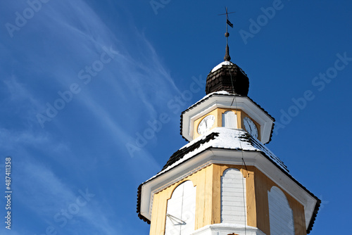 A yellow clock tower of an old church with blue sky and white thin cloud on a background