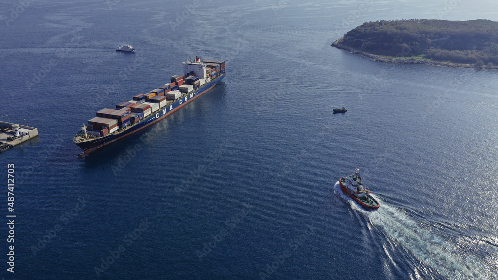 Aerial drone top down photo of tow - tug boat assisting by pulling or pushing container ship to anchor in logistics terminal port