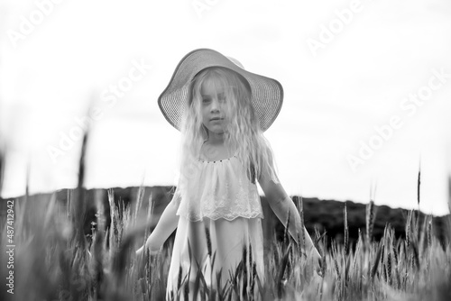 Adorable little girl playing in the wheat field on a warm summer day