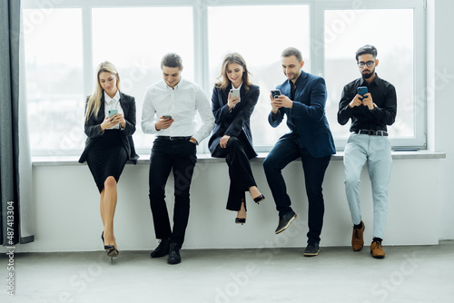 business colleagues with their smartphones. laptop, tablet, sitting in the office hallway