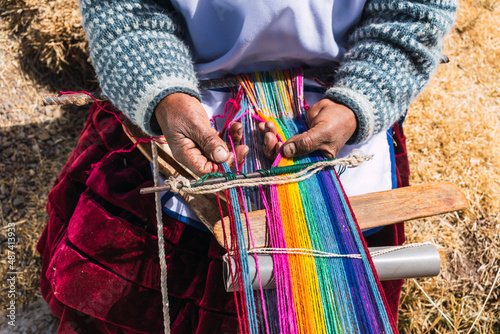 poor indigenous adult woman artisan with blue mask and typical ancestral costume weaving in times of covid-19 pandemic on a sunny day in the Andes mountain range