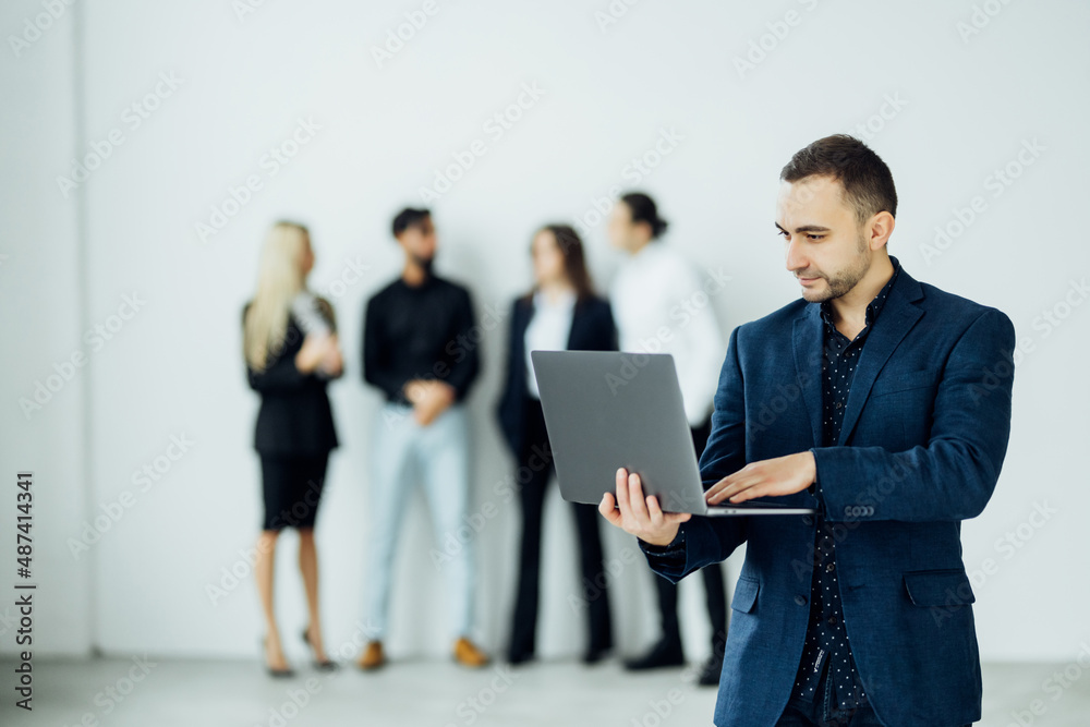 Young business man working on laptop in the office in front of their team Young business man working on laptop in the office in front of their team
