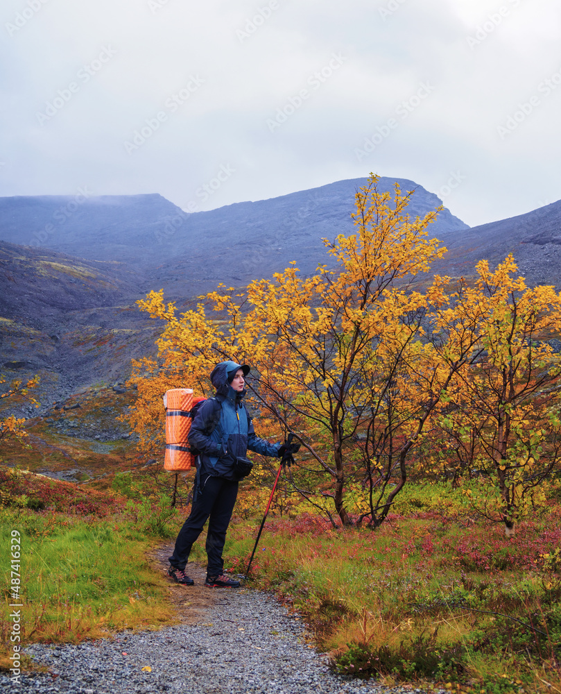 A woman with a backpack in the autumn season walks along a path in the mountains on a rainy day.