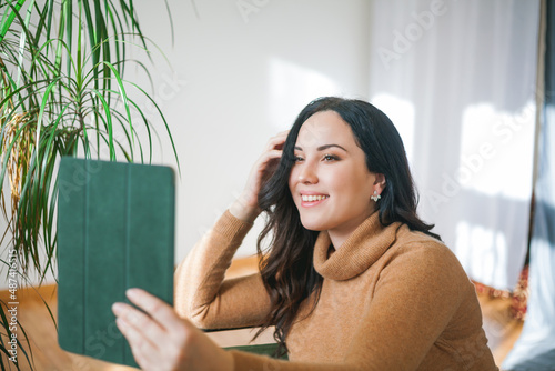 Business portrait of a young woman in comfortable casual clothes with a tablet in her hands. Stylish woman works at home. Online work, video call. Home office.