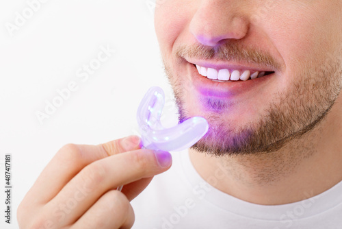A man holds in his hand an ultraviolet lamp for home teeth whitening. A snow-white smile after bleaching.