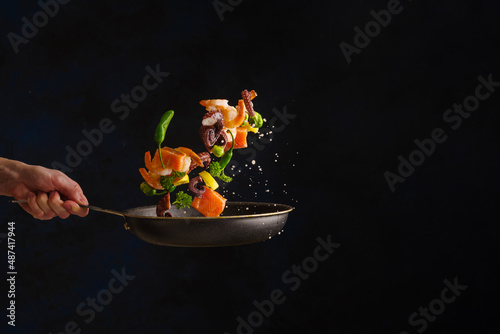 Assorted seafood in a frying pan in a state of levitation on a black background. The concept is cooking seafood, restaurant cuisine recipes. Hotel, restaurant, recipe book.