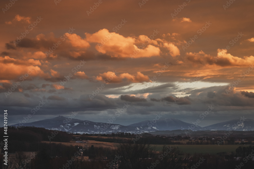 colorful sunset clouds over the countryside in czech republic with snow and mountains in the background on a winter day
