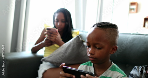 Casual African family relaxing at home sofa using technology. Black parents and kids each using their tech devices bubbles
