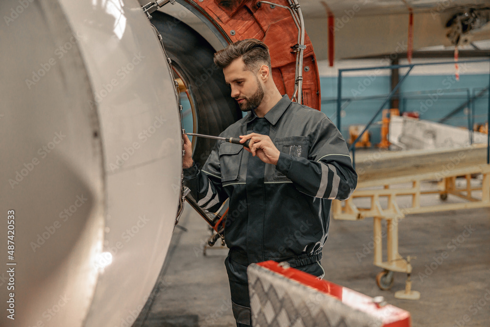 Bearded man airline maintenance technician using screwdriver while repairing aircraft