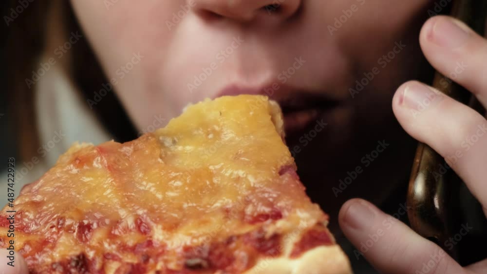 The woman is eating pizza and talking on the phone. Close-up on the lower part of the face - mouth. A middle-aged woman, forty years old. Dark background. The woman is eating pizza and talking on the phone. Close-up on the lower part of the face - mouth. A middle-aged woman, forty years old. Dark background.