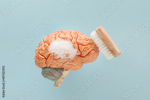 Minimal abstract scene with soapy human brain model and scrubbing brush on isolated pastel blue background. Mental health, brain fog or health care treatment. Cleansing or brainwashing concept.