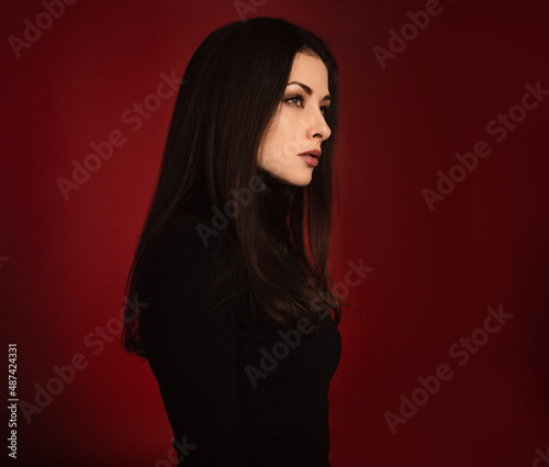 Beautiful confident serious business woman in black sweater posing with hand under the face on dark red background with empty copy space. Closeup profile