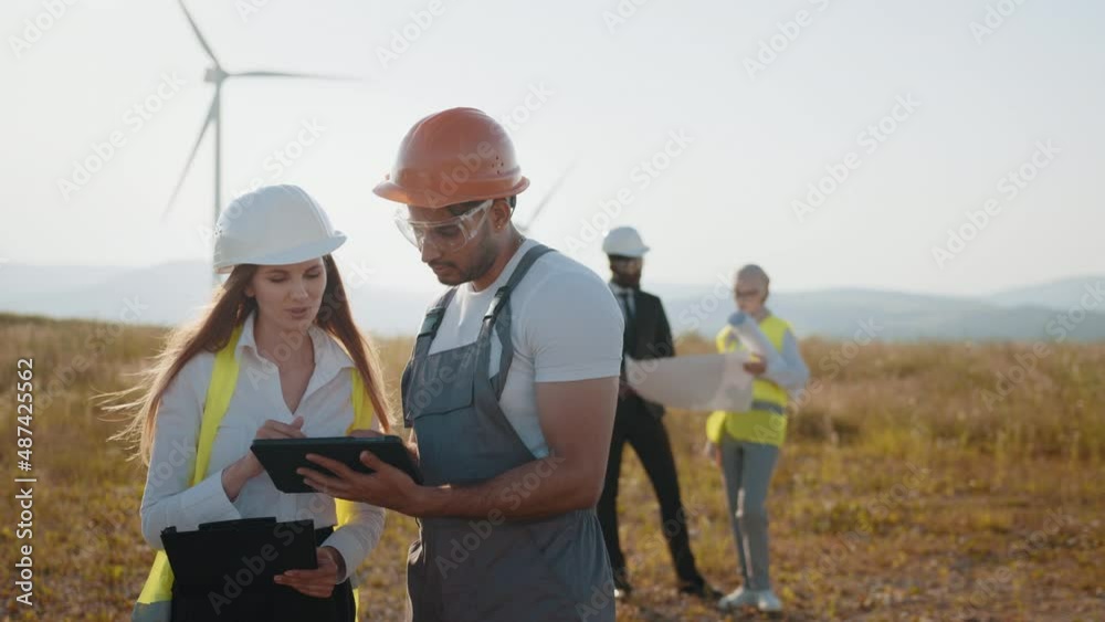 International team of business partners standing together among wind turbines and examining blueprints. Group of professionals cooperating for producing clean eco friendly energy. Eco electric power International team of business partners standing together among wind turbines and examining blueprints. Group of professionals cooperating for producing clean eco friendly energy. Eco electric power