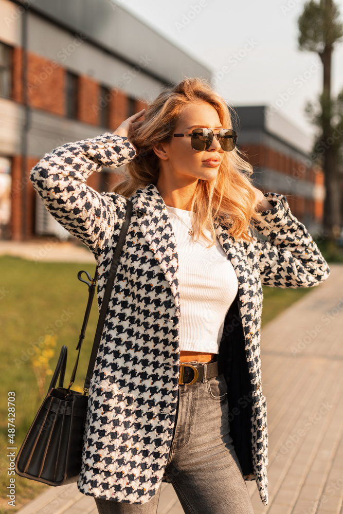 Fashion young blonde woman in fashion summer outwear with bad walks on the street at sunset.