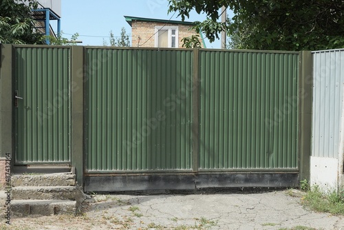 one big green closed metal gate and door on a rural street