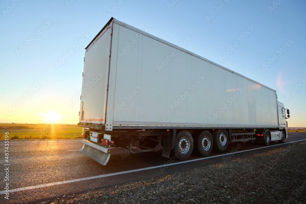 Semi-truck with cargo trailer driving on highway hauling goods in evening. Delivery transportation and logistics concept