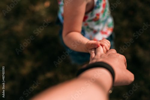 A toddler holds her mother's hand while on a walk in the summer