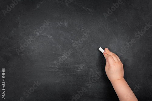 Child hand writing with chalk on empty school blackboard, copy space