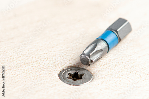 Screw the screw into the board. Furniture production, a screwdriver twists a self-tapping screw into a board. Several silver screws lie on the desktop