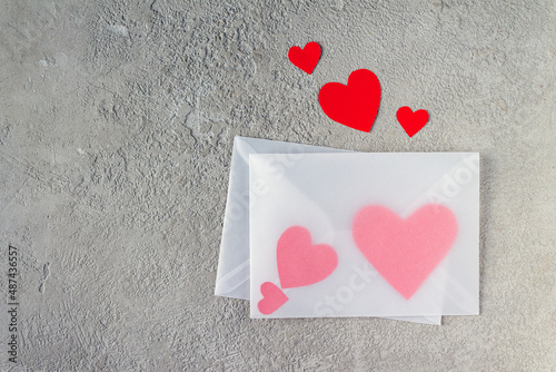 transparent envelopes with red paper hearts on a gray background