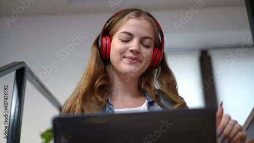 Front view carefree teenage girl dancing listening to music in headphones from laptop playlist. Happy relaxed Caucasian teenager enjoying hobby at home indoors on weekend. Leisure concept photo