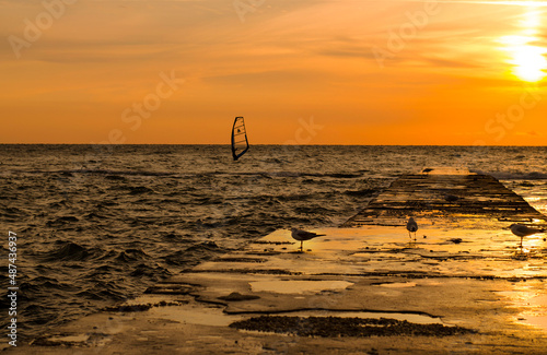 Silhouettes of windsurfers in the sea at the sunrise. People are doing sports at the dawn. Orange colours of the sunrise makes the sae look majestic.