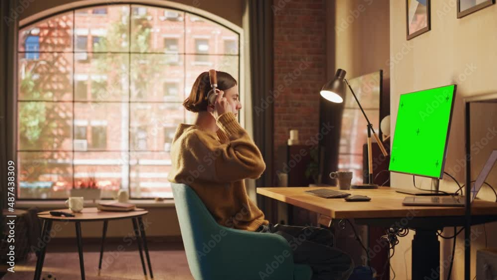 Young Handsome Man Working from Home on Desktop Computer with Green Screen Mock Up Display. Creative Male Checking Social Media, Browsing Internet. Urban City View from Big Window.