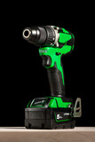 a cordless screwdriver stands on a wooden table on a black background. Cordless drill with lithium-ion battery in green. Professional tool for drilling holes and driving screws.