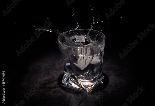Splashes of water from a piece of ice falling into a transparent glass with a black background