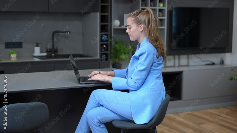 Side view concentrated busy freelancer in formal suit typing on laptop keyboard sitting in kitchen at home. Confident intelligent Caucasian young woman messaging online surfing Internet indoors Side view concentrated busy freelancer in formal suit typing on laptop keyboard sitting in kitchen at home. Confident intelligent Caucasian young woman messaging online surfing Internet indoors