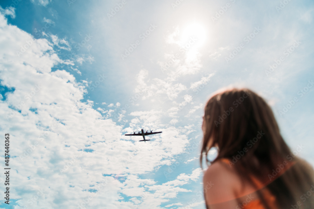 A girl watches a plane fly overhead - obrazy, fototapety, plakaty 