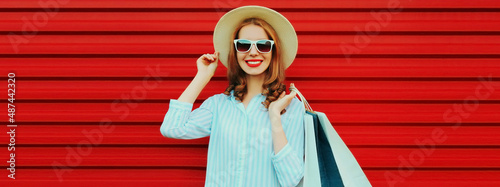Portrait of happy smiling young woman with shopping bags wearing straw hat and shirt on colorful red background © rohappy