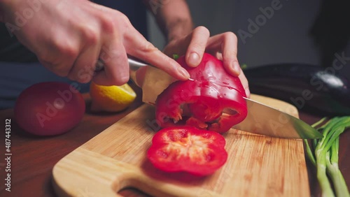 Person slicing a red pepper on a wooden board in slow-motion