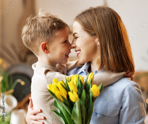 Young  woman mother with flower bouquet embracing son while getting congratulations on Mother's day
