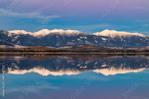 Winter landscape at sunset. Snow-capped mountains reflected in the lake. Liptovska Mara dam with the Western Tatras mountain in the background, Slovakia, Europe.