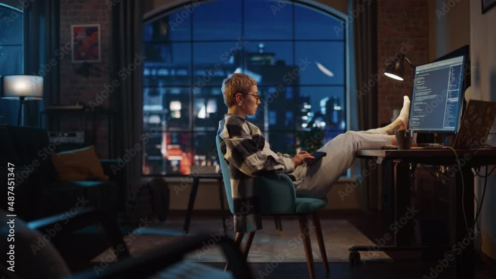 Young Woman Writing Code on Computer in Stylish Loft Apartment in the Evening. Creative Female Wearing Cozy Clothes, Resting Feet on Table and Using Wireless Keyboard. Urban City View from Big Window. Young Woman Writing Code on Computer in Stylish Loft Apartment in the Evening. Creative Female Wearing Cozy Clothes, Resting Feet on Table and Using Wireless Keyboard. Urban City View from Big Window.