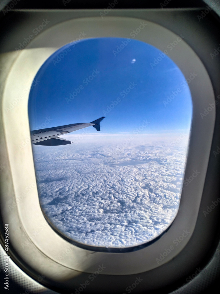 The view from the plane window on a cloudy sky in winter. Cabin window, snow, blue sky, plane wing, frozen plane window, flying. View on earth from a plane. The view from the plane window on a cloudy sky in winter. Cabin window, snow, blue sky, plane wing, frozen plane window, flying. View on earth from a plane.