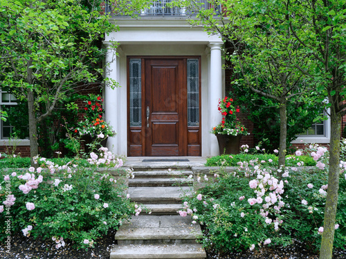 House and garden with rose bushes and flagstone steps leading to elegant wood grain front door