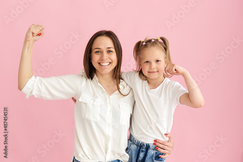 Mom and daughter show their muscles and strength in the studio on a pink background