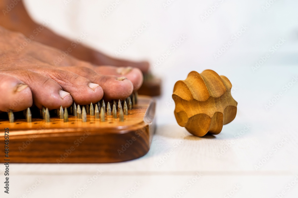 Feet stand on a board with nails and one wooden massager nearby. Pain while practicing standing on nails Feet stand on a board with nails and one wooden massager nearby. Pain while practicing standing on nails