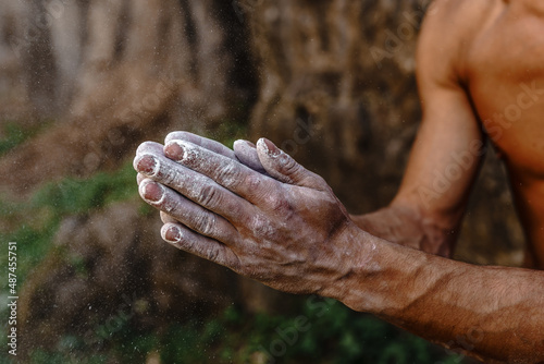 Outdoor rock climbing. The hands of a tanned athlete are smeared with magnesia powder close-up on a forest background