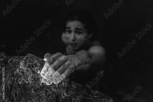 Black and white portrait of an Asian man who is engaged in rock climbing. Climber holding on to a rock with one hand. Climber's hands in white powder of magnesia.