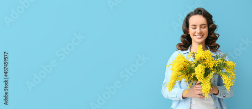 Beautiful young woman with mimosa flowers on blue background with space for text