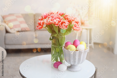 Vase with tulips and Easter eggs on table in room